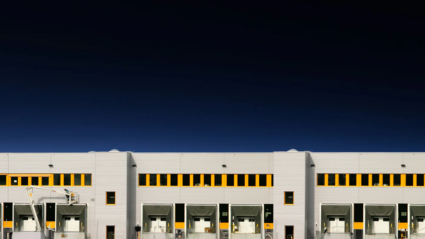 Row of warehouse dock doors with yellow-and-black bumpers under a deep blue dusk sky