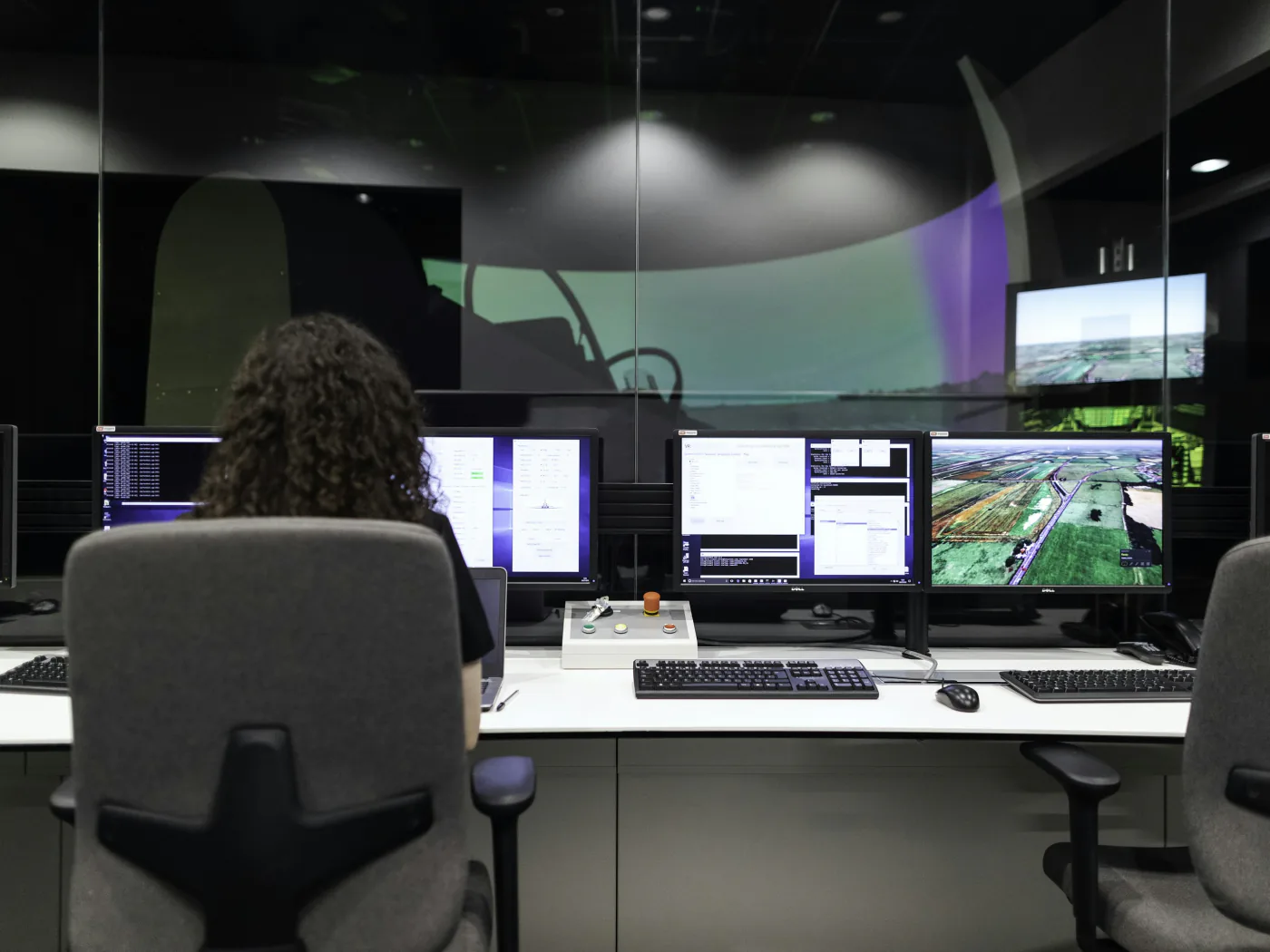 Operator seen from behind at a control-room desk spanning four monitors of maps and telemetry